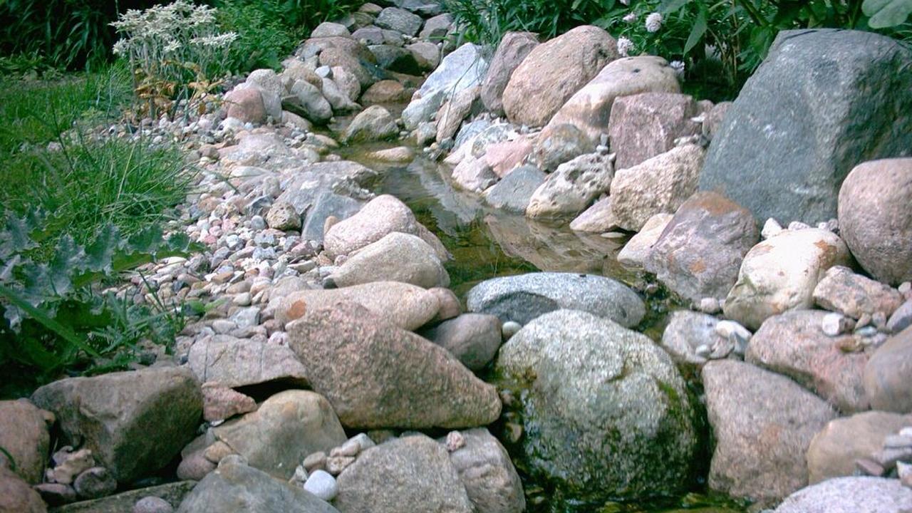 Nahansicht eines kleinen Bachlaufs im Garten mit großen und kleinen Steinen nach dem Teichbau